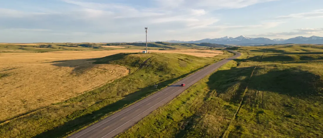 Aerial photo of a lone highway through prairie hills with a cell tower on a hill and mountains in the distance